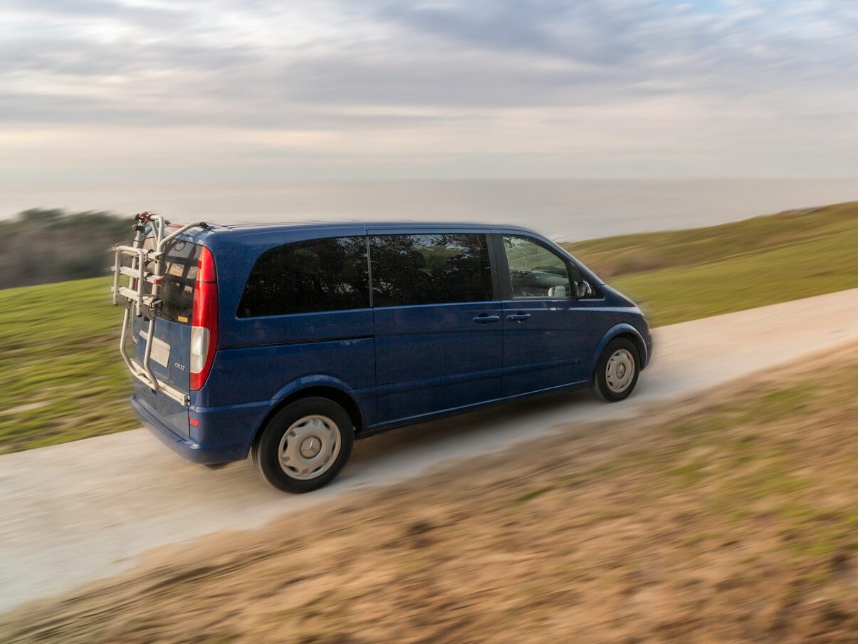 a blue van driving down a dirt road