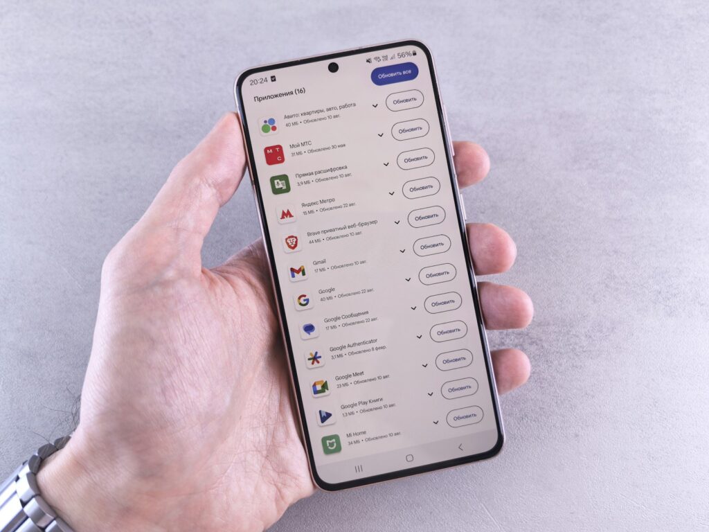 A hand holds a phone displaying apps.